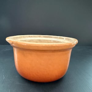 May include: A round, terracotta-coloured ceramic bowl with a smooth, glazed finish. The bowl features a wide, slightly flared rim and a deep, open interior. The exterior surface displays a consistent, warm orange-brown hue with subtle tonal variations.
