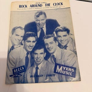 May include: A vintage sheet music cover for Rock Around The Clock by Bill Haley and His Comets. The blue and white print features a group portrait of the band members, the song title, and the Decca Records and Myers Music logos.