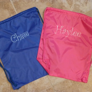 May include: Two drawstring bags, one blue and one pink. The blue bag has the name "Chase" embroidered in white, while the pink bag has "Haylee" embroidered in white. Both bags have matching drawstring cords.