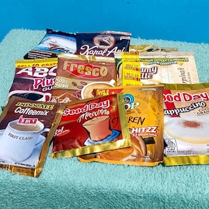以下が含まれることがあります： Kapal Api、Fresco、ABC Plus、Indocafe Coffeemix、Good Day Mocaccino、Top Coffee Hitzz、Good Day Cappuccinoなどのブランドを含む、様々なインスタントコーヒーの小袋のコレクション。カラフルなパッケージにコーヒーの画像が印刷されています。