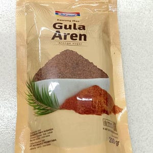 May include: A tan plastic pouch of Indomaret Kawung Mas Gula Aren arenga sugar. The packaging features a graphic of a white bowl filled with dark brown granulated sugar, a pile of loose sugar, and a green palm leaf. The net weight is 200 grams.