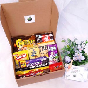Puede incluir: Una caja de regalo de cartón marrón llena de varios aperitivos, incluyendo patatas fritas Chitato, barquillos Nabati, leche Ultra Milk, galletas Selimut, galletas Nextar, Chocolatos, piruletas Milkita y gominolas Yupi.