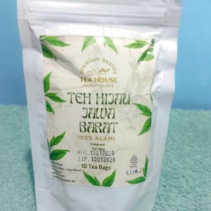 Könnte beinhalten: Ein weißer Standbeutel mit 10 Teebeuteln. Das Etikett zeigt grüne Blattillustrationen, den Text "TEA HOUSE MADE WITH LOVE", "TEH HIJAU JAWA BARAT", "100% ALAMI", "10 Tea Bags" sowie ein "HALAL"-Zertifizierungslogo mit Herstellungs- und Verfallsdatum.