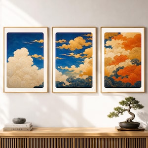 May include: A set of three framed vertical wall art prints featuring stylized clouds. The first print shows gold clouds against a deep blue sky. The second print displays gold and blue clouds. The third print depicts vibrant orange and dark blue clouds.