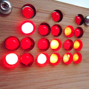 May include: A wooden board with a grid of red and yellow LED lights. The lights are arranged in a pattern, with some lights on and some lights off.