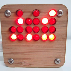 May include: A wooden board with a grid of red LED lights, some of which are lit. The board is connected to a USB cable.