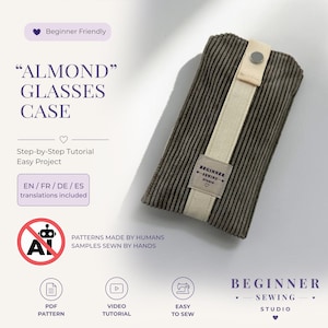 Könnte beinhalten: Ein dunkelgraues Brillenetui aus Kord mit einem cremefarbenen Stoffriemen und einem silbernen Metalldruckknopf. Ein rechteckiges Etikett auf dem Riemen trägt die Aufschrift BEGINNER SEWING STUDIO. Der Text ALMOND GLASSES CASE ist links zu sehen.