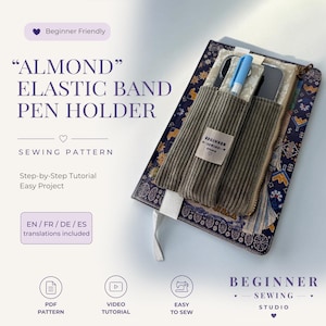 Può includere: Un portapenne in velluto a coste verde oliva con fascia elastica fissato a un taccuino blu scuro con motivi. Il supporto presenta una piccola etichetta in tessuto con la scritta BEGINNER SEWING STUDIO e contiene una penna azzurra. Il testo ALMOND ELASTIC BAND PEN HOLDER è visibile.