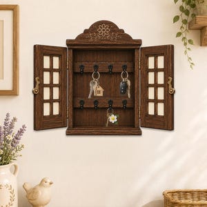 May include: A dark brown wooden wall-mounted key cabinet with two hinged doors featuring a grid pattern. The cabinet has an arched top with a floral carving, six black metal hooks, and holds three sets of keys with various keychains.