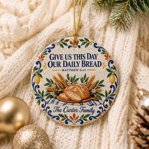Puede incluir: Un adorno de cerámica redondo con el texto "Give Us This Day Our Daily Bread" y "Matthew 6:11" sobre una ilustración de pan en rodajas, espigas de trigo y limones. El borde tiene motivos florales azules y verdes, con "The Carter Family" en la parte inferior.