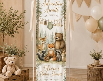 Peut inclure: Une bannière en tissu verticale avec le texte Adventure Awaits, Welcome To, Olivia's Baby Shower et October 11, 2026. Le design présente des illustrations d'un cerf, d'un ours, d'un renard, d'un raton laveur et d'un lapin dans une forêt.