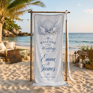 May include: A vertical fabric wedding welcome sign featuring a light blue and white striped pattern. The top displays a blue illustration of seashells and a starfish. The text reads: Welcome to our Wedding, Emma & James, August 22, 2026.