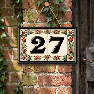 May include: A rectangular house number sign featuring the number 27 in bold black font on a cream background. The sign is framed by a decorative border of red tulips and green leaves on a cream tile base, enclosed in a thin black frame.