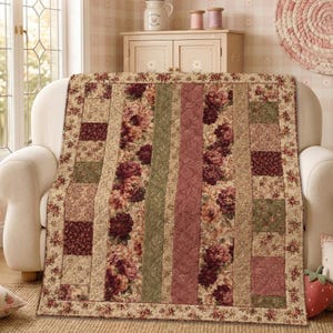 May include: A rectangular quilt featuring a patchwork design of vertical stripes and squares. The fabric displays floral patterns in shades of burgundy, sage green, and cream. The quilt has a quilted texture and a border with a small floral print.