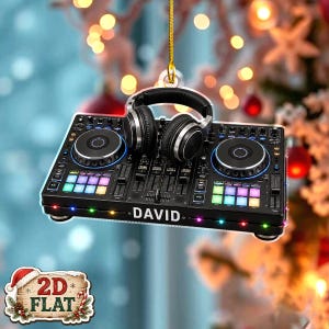 May include: A black DJ controller ornament featuring two circular jog wheels, colourful square pads, and a pair of black headphones resting on top. The front edge of the controller displays the name DAVID in white capital letters.