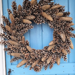 May include: A brown pine cone wreath hangs on a blue door. The wreath is made of many pine cones, all of which are brown and have a natural, rustic look.