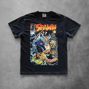 Könnte beinhalten: Ein schwarzes Kurzarm-T-Shirt mit einem Grafikdruck des Spawn-Comic-Covers Ausgabe 34. Das Design zeigt das Wort Spawn in großen gelben und roten Buchstaben sowie eine detaillierte Illustration einer Figur in einer blauen Jacke.