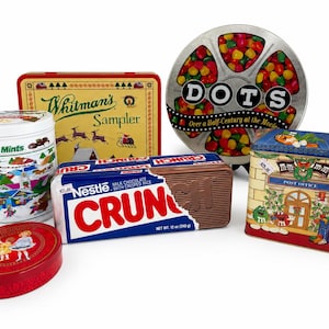 Op de afbeelding: Assortiment van vintage snoeptins en -dozen, waaronder Whitman's Sampler, Junior Mints, Nestle Crunch en een Dots snoepcontainer. De tins hebben kleurrijke ontwerpen en tekst, met een rode ovale tin op de voorgrond.