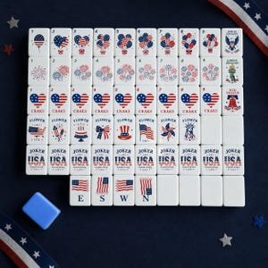 May include: A set of white rectangular mahjong tiles featuring red, white, and blue patriotic graphics including balloons, fireworks, hearts, the Statue of Liberty, and American flags. Each tile displays specific numbers, text, or symbols.