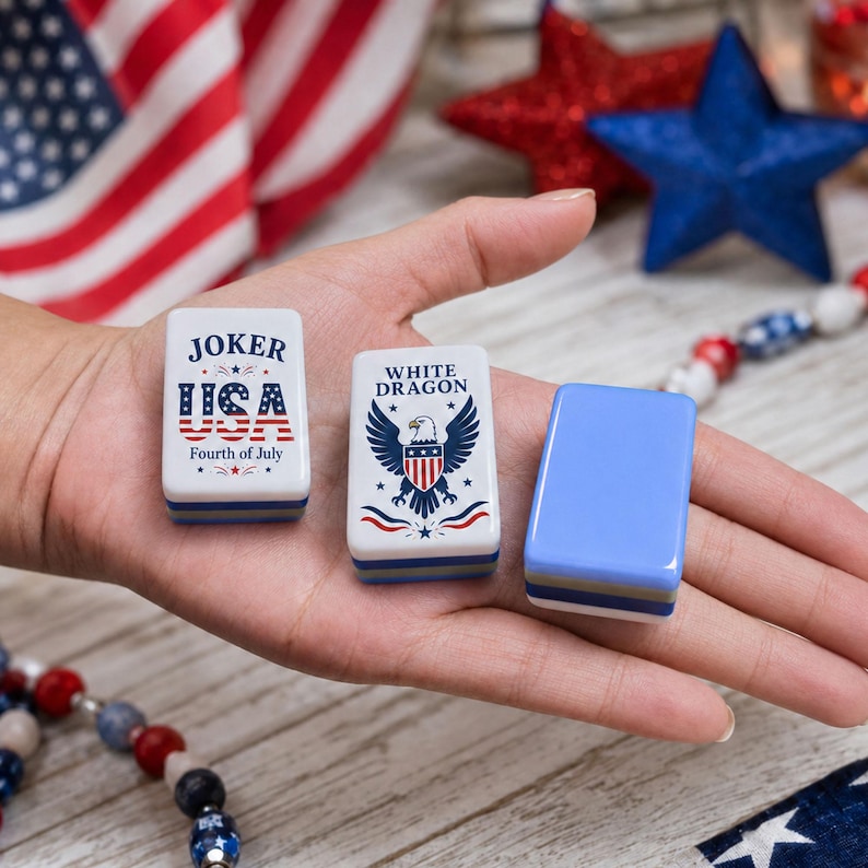 May include: Three rectangular mahjong tiles with rounded corners. One tile features the text JOKER USA Fourth of July with a flag pattern. Another tile displays the text WHITE DRAGON with a bald eagle graphic. The third tile is solid light blue.