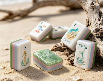 Puede incluir: Un conjunto de fichas de mahjong rectangulares con coloridas ilustraciones de temática playera. Una ficha muestra a una surfista con la letra S, otra muestra chanclas con el texto FLOWER y una tercera muestra una cola de ballena con el texto JOKER.