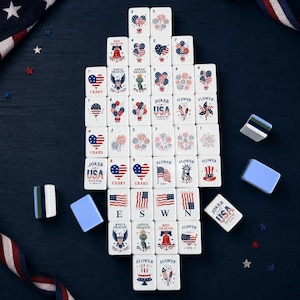 May include: A set of white mahjong tiles featuring red, white, and blue patriotic designs including American flags, fireworks, hearts, eagles, the Statue of Liberty, and text reading Joker USA Fourth of July, arranged in a vertical rectangular formation.