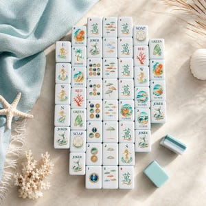 May include: A set of white rectangular mahjong tiles featuring colorful illustrations of mermaids, beach umbrellas, coral, seashells, and soap, alongside traditional Chinese characters and numbers. Two plain tiles are placed separately nearby.