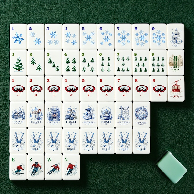 Pu&ograve; includere: Un set di tessere Mahjong bianche con illustrazioni a tema invernale, tra cui fiocchi di neve, alberi di pino, occhiali da sci e una funivia rossa. Le tessere sono disposte su una superficie verde, con una tessera verde abbinata.