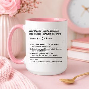 May include: A white ceramic mug with a pink handle and interior, featuring black printed text that defines a DevOps engineer. The text reads: DEVOPS ENGINEER BUILDS STABILITY, Noun (n.) - Rose, followed by three numbered points and See Also: Leader, Problem Solver, Steady Hand.