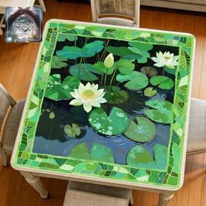 Lotus clear pond mahjong mat displayed on a square table, featuring an original water garden design with white lotus flowers, layered lily pads, rippling dark water, and a bright green mosaic style border.