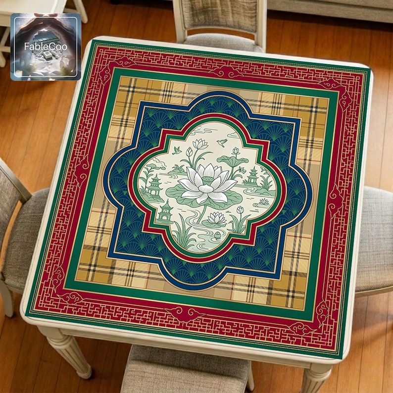 Asian-style mahjong mat displayed on a square home table, featuring an original oriental-inspired lotus garden design with blooming white lotus flowers, lotus leaves, peaceful water details, pavilion architecture, flying birds, a classic window-shaped central frame, fan-pattern background, plaid accents, and richly decorative eastern-style borders in burgundy, deep green, royal blue, khaki gold, ivory, and soft green tones.