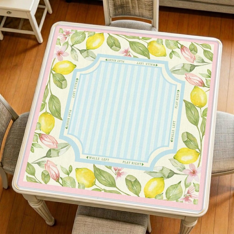 Lemon mahjong mat displayed on a square table, featuring bright yellow lemons, soft green leaves, pink blossoms, and a fresh light blue striped center.