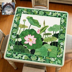 Pink lotus pond mahjong mat displayed on a square table, featuring an original botanical water garden design with blooming pink lotus flowers, layered green lotus leaves, unopened buds, and an ornate leafy green border.