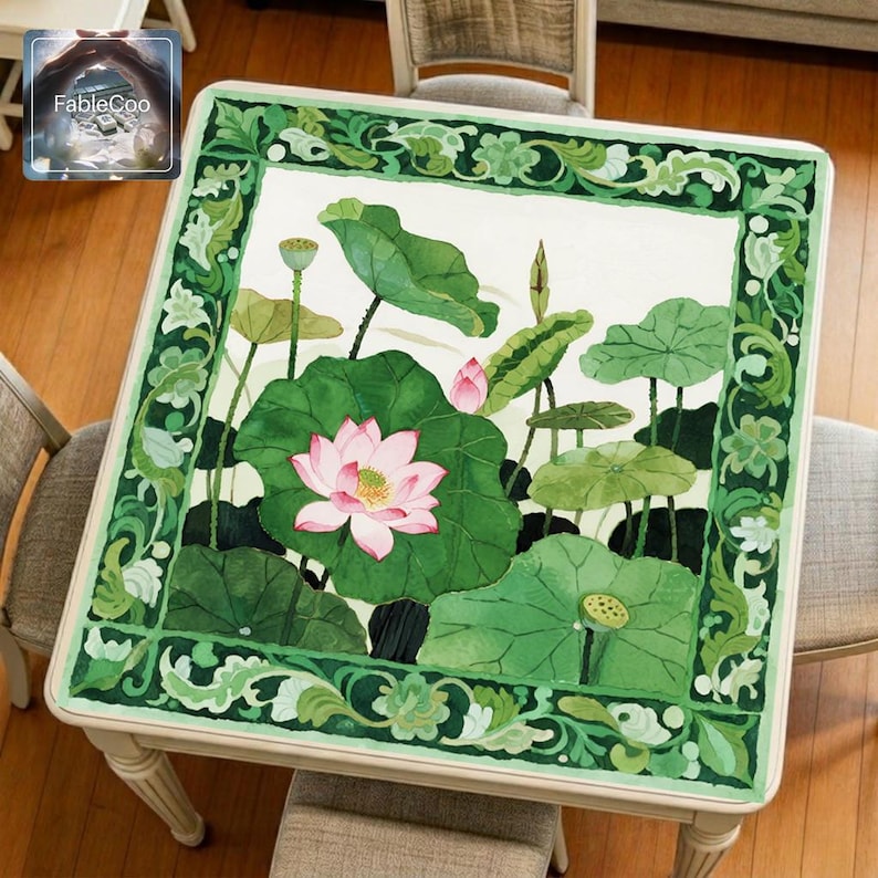 Pink lotus pond mahjong mat displayed on a square table, featuring an original botanical water garden design with blooming pink lotus flowers, layered green lotus leaves, unopened buds, and an ornate leafy green border.