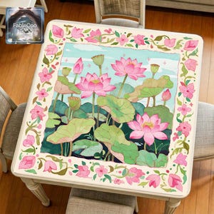 Pink lotus mahjong mat displayed on a square table, featuring an original floral pond design with blooming lotus flowers, lotus leaves, seed pods, soft sky blue water background, and a decorative pink blossom border.