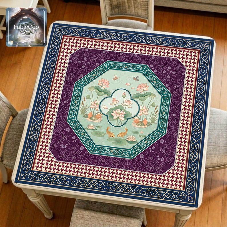 Asian-style mahjong mat displayed on a square home table, featuring an original oriental-inspired lotus pond design with blooming lotus flowers, lotus leaves, koi fish, small birds, butterflies, gentle water ripples, an octagonal window-style frame, fan-pattern detailing, houndstooth accents, and elegant decorative borders in navy blue, plum purple, teal green, soft mint, ivory, and gold tones.