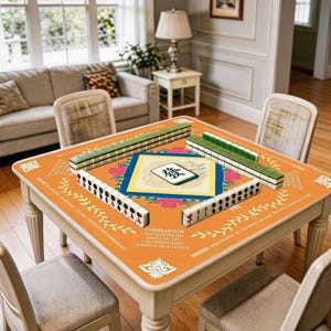 Orange minimalist style mahjong mat displayed on a square table, featuring a clean geometric layout, centered mahjong-inspired artwork, and bright decorative border details.