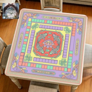 Chinese koi fish mahjong mat displayed on a square home table, featuring an original new Chinese-style design with elegant koi fish circling a central lotus flower, surrounded by auspicious clouds, geometric knot details, and decorative key-pattern borders in soft lavender, mint green, butter yellow, and peach pastel tones.