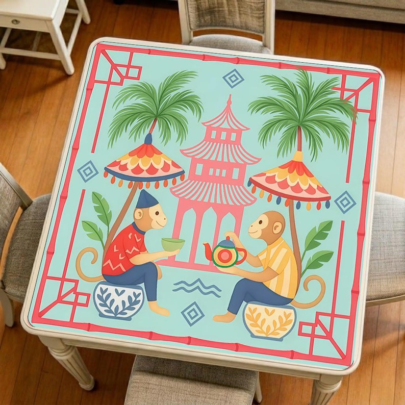 Tropical monkey mahjong mat displayed on a square table, featuring two playful monkeys, palm trees, parasols, and a colorful pavilion-inspired design.