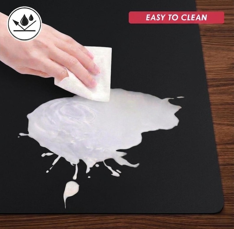 May include: Black surface with a white liquid spill being wiped with a white cloth. The image includes a graphic of water droplets and the text "EASY TO CLEAN" in a red rectangle.