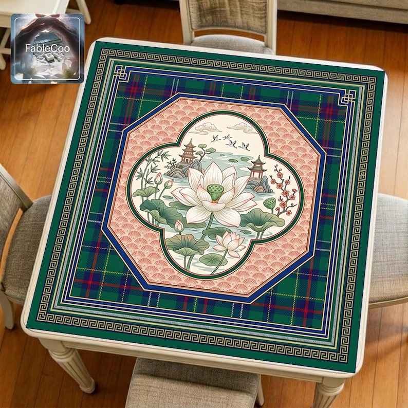 Asian-style mahjong mat displayed on a square home table, featuring an original oriental-inspired lotus pond scene with blooming lotus flowers, layered lotus leaves, traditional pavilions, flying birds, bamboo details, soft water elements, decorative window-style framing, Greek key borders, and tartan accents in deep green, navy blue, coral pink, gold, ivory, and muted natural tones.
