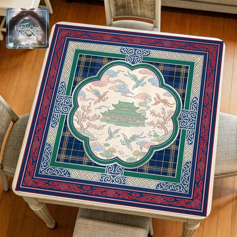 Asian palace-style mahjong mat displayed on a square home table, featuring an original oriental-inspired design with a central palace building, flying cranes, flowering branches, lotus details, soft cloud motifs, and layered decorative borders in deep blue, teal green, red, and ivory tones.