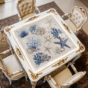 Ocean-themed mahjong mat displayed on a square table, featuring coral branches and starfish in elegant blue and ivory coastal tones.