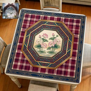 Asian-style mahjong mat displayed on a square home table, featuring an original oriental-inspired lotus design with blooming pink lotus flowers, lotus leaves, layered octagonal geometric framing, classic plaid background, Greek key accents, and elegant gold borders in burgundy red, navy blue, deep green, ivory, and blush pink tones.