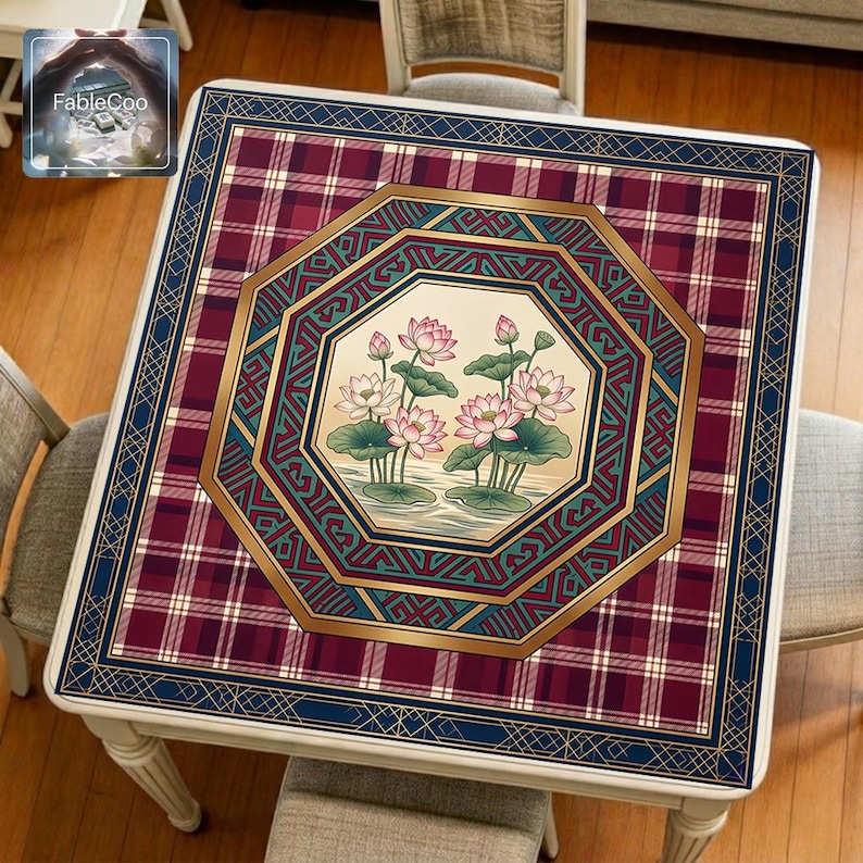 Asian-style mahjong mat displayed on a square home table, featuring an original oriental-inspired lotus design with blooming pink lotus flowers, lotus leaves, layered octagonal geometric framing, classic plaid background, Greek key accents, and elegant gold borders in burgundy red, navy blue, deep green, ivory, and blush pink tones.