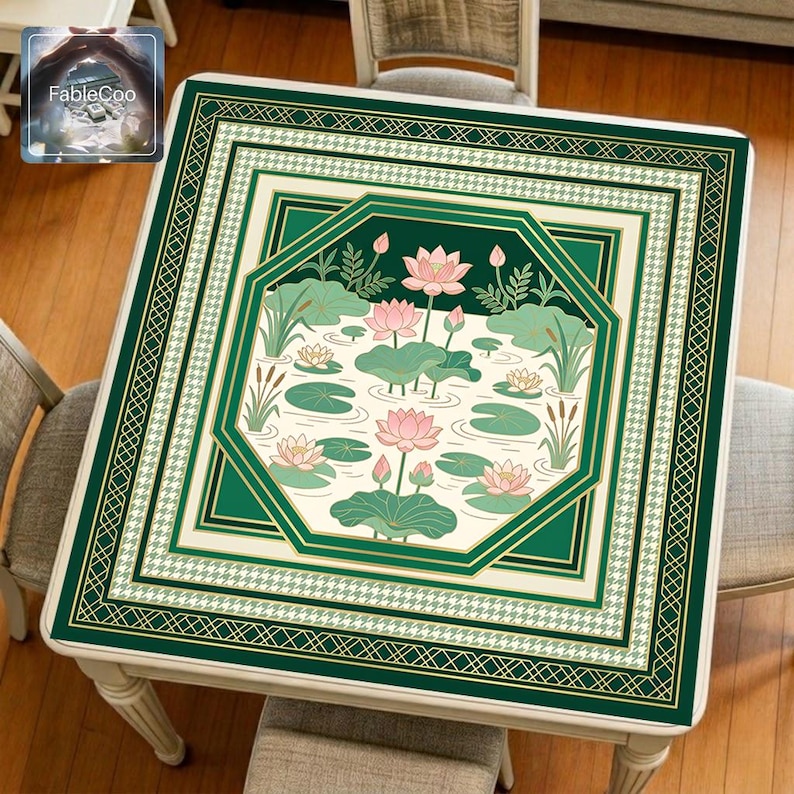 Asian-style mahjong mat displayed on a square home table, featuring an original oriental-inspired lotus pond design with blooming pink lotus flowers, broad lotus leaves, lily pads, reeds, flowing water lines, layered octagonal framing, and elegant gold borders in deep green, ivory, pale pink, soft jade, and muted gold tones.
