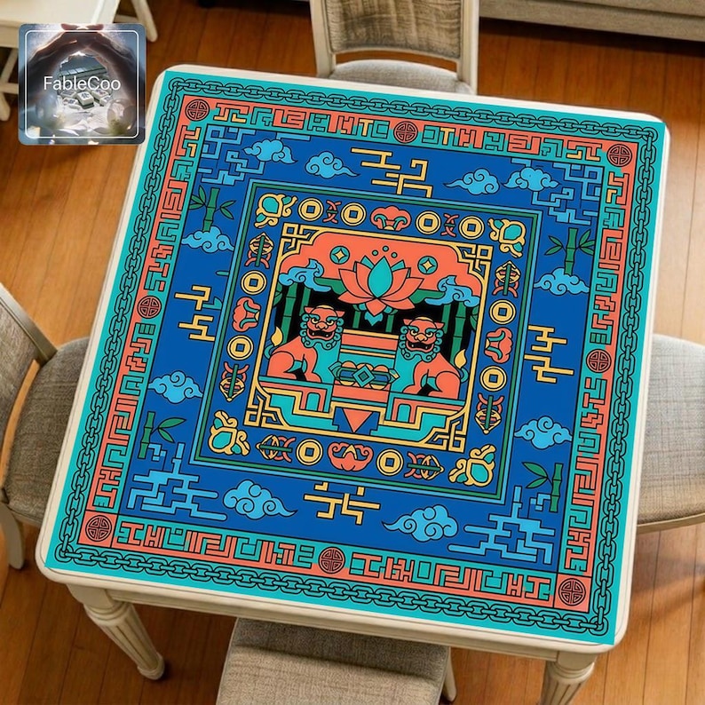 Chinese guardian lion mahjong mat displayed on a square home table, featuring an original new Chinese-style design with two protective lions flanking a central treasure motif beneath a blooming lotus, surrounded by auspicious clouds, bamboo accents, symbolic ornaments, and traditional geometric key-pattern borders in vivid royal blue, turquoise, coral orange, and golden yellow tones.