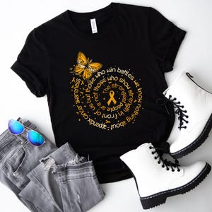 May include: A black t-shirt featuring a yellow butterfly and an orange awareness ribbon surrounded by circular text that reads: The strongest people are not those who show strength in front of us but those who win battles we know nothing about.