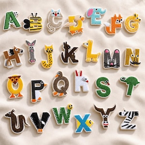 Peut inclure: Lettres de l'alphabet brodées avec des motifs d'animaux. Chaque lettre représente un animal différent, notamment une abeille, un chat, un renard, un cheval et un zèbre. Les lettres sont de couleurs variées, comme le vert, le jaune, l'orange et le marron. Les lettres sont sur un fond crème.