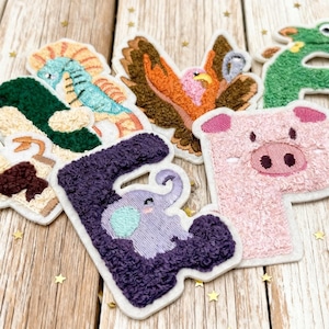 Peut inclure: Écussons en tissu brodé en forme de lettres et d'animaux. Les écussons comprennent un hippocampe, un aigle, une grenouille, un cochon et un éléphant. Les écussons sont de différentes couleurs, dont le vert, le violet, le rose et l'orange, avec des bordures blanches.